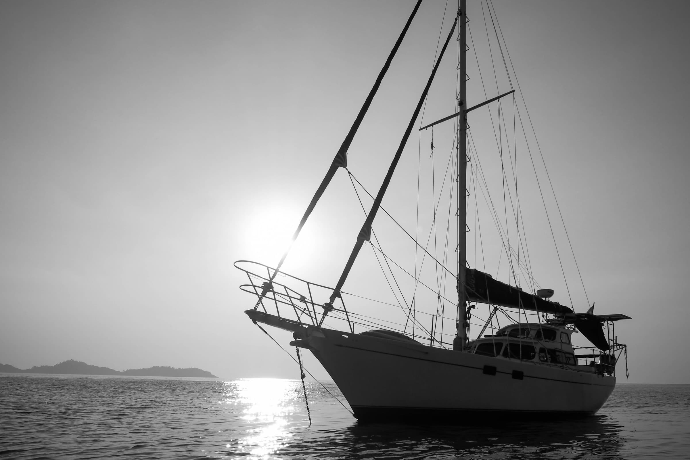 A ketch lying at anchor in still water at dawn.
